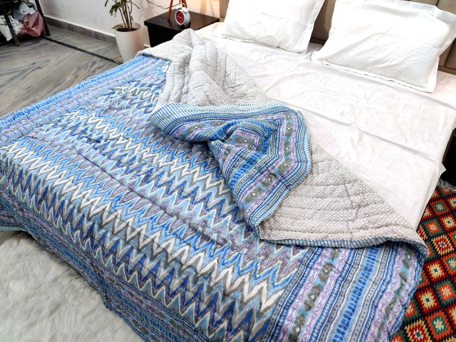 Jaipuri cotton quilt double bed in vibrant blue patterns spread over a white bed with pillows